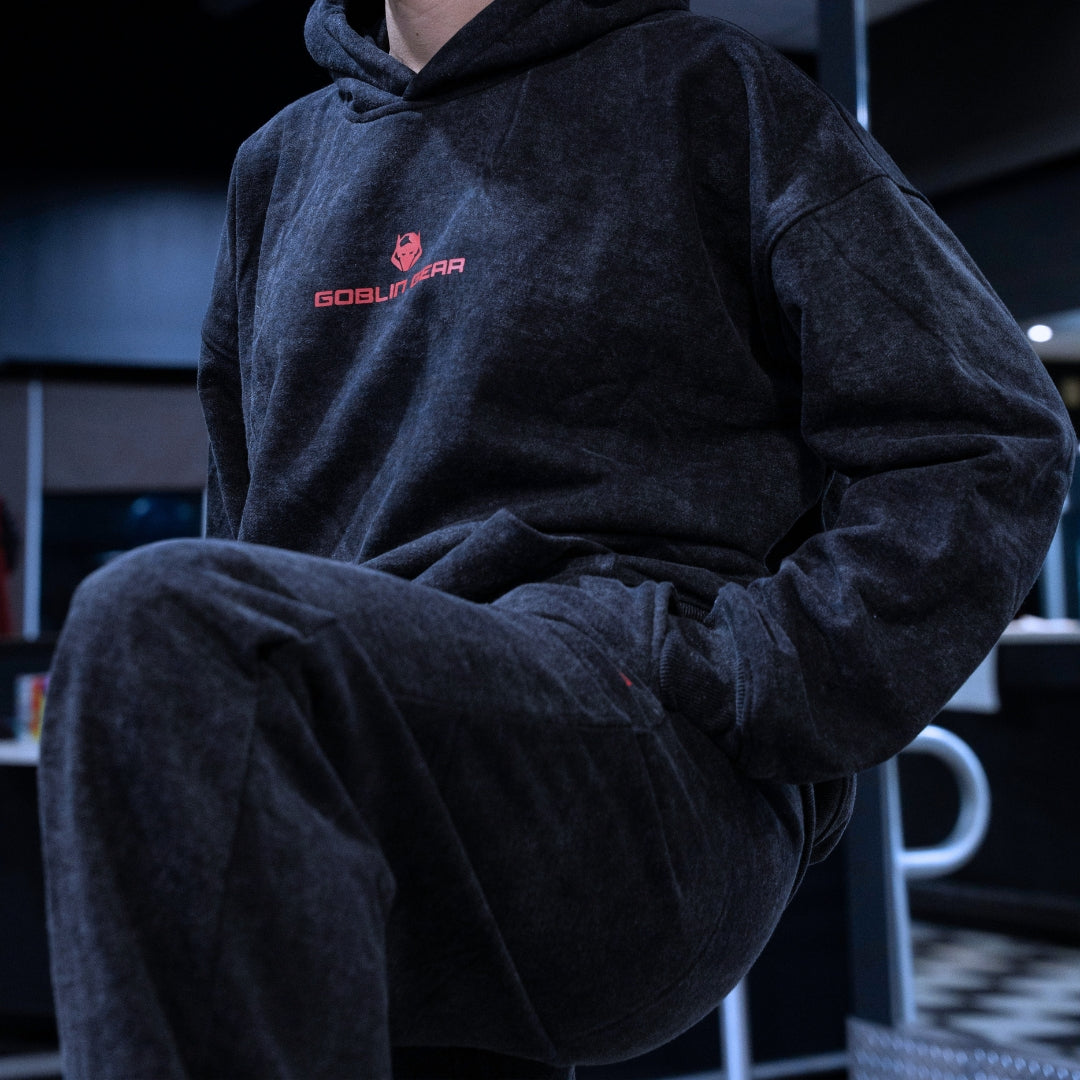 Goblin Gear Acid Wash Hoodie – person wearing a dark hoodie with a logo sitting in a room