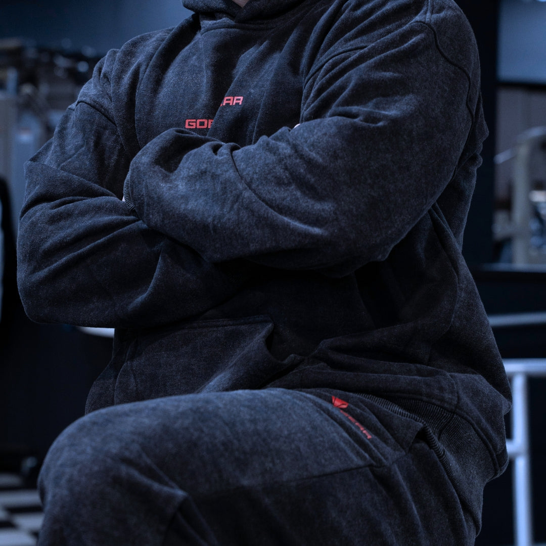 Goblin Gear Acid Wash Hoodie – person wearing a dark gray hoodie with red branding sitting in a dimly lit room